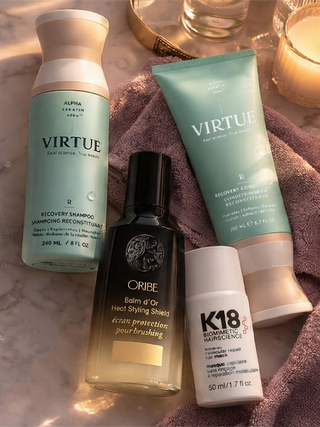 Set of hair care products including shampoo, serum, and cream on a towel with a candle in the background.