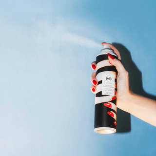 Hand holding a striped hair spray can against a blue background