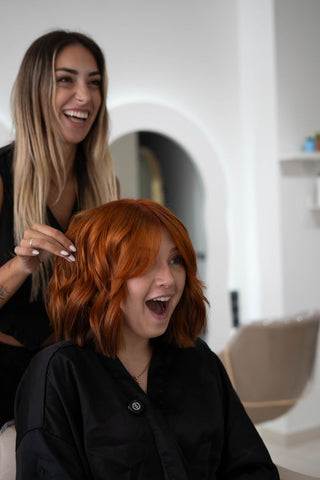 Two women in a salon setting with one smiling and the other adjusting hair.